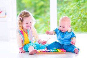 Two little children - cute curly toddler girl and a funny baby boy, brother and sister playing music, having fun with colorful xylophone at a window; kids early development class