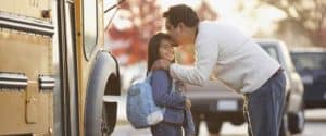Father kissing daughter goodbye in front of school bus